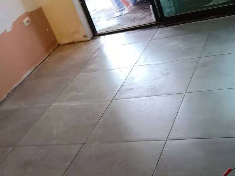 客廳地磚鋪貼：鋪貼的工具包括橡膠錘和粘結(jié)劑。在進(jìn)行施工之前先把所需要的這些材料都整理好放在一旁備用；基層的處理工作對(duì)瓷磚的平整度有很大的影響，對(duì)于基層要做好清潔工作，還有找平工作。放樣：在進(jìn)行瓷磚的鋪貼工作之前還事先找好垂直線，這樣可以在鋪貼的時(shí)候找到瓷磚的水平線，讓瓷磚鋪貼的更加的平整。粘結(jié)劑加水?dāng)嚢杈鶆颍o置10分鐘之后就可以使用。將瓷磚表面的浮灰清除，再在瓷磚背面均勻的涂抹上粘結(jié)劑，按照預(yù)鋪的順序?qū)⒋纱u鋪貼在地面上，最后用橡膠錘輕輕拍打至服帖齊整。
