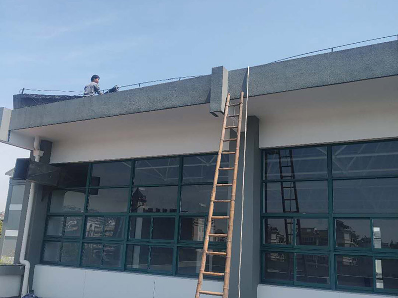 學校屋頂防水：屋頂做防水前，要先對需要防水施工的屋頂基層進行清潔，因為很多防水施工中要避免一些雜物、塵土等，打掃干凈了更有利于防水施工效果。屋頂防水施工就與室內防水施工差不多，室內的地漏、水管位置等都要重點涂刷，而屋頂中的水落口、女兒墻、檐口、陰陽角等位置也要先進行針對性的施工，也被稱為附加層施工。屋頂施工防水需要不少材料，特別是防水用的改性瀝青卷材、防水涂料等等，先對基層鋪貼一層防水卷材，其厚度要符合要求，尺寸根據屋頂面積進行裁剪。卷材一般歐式用熱熔的方式來鋪貼，也就是需要借助火焰噴槍來加熱進行滾鋪、粘貼，卷材從檐口處與屋脊平行的方向由下而上進行鋪貼。卷材的各個搭接處都要用噴槍來加熱粘結牢固，并且在邊緣末端收頭處要用密封膏來嵌填嚴密好才行。卷材鋪貼好后，要再一次進行屋頂清潔，保障干凈、干燥的施工環境，這時候就可以進行第一層的防水涂料刷涂了，第一遍一定要涂滿，不能出現遺漏、裂紋、氣泡、黏合不牢固等現象。